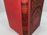 an old book with a red cover sitting on top of a white table