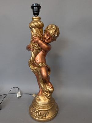 une statue en or représentant un enfant tenant une lampe, posée sur une table
