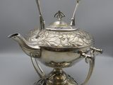 a silver teapot with a black handle on a stand