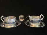 deux tasses et soucoupes en métal argenté, accompagnées de cuillères, posées sur un fond noir