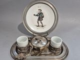 un plateau en argent avec des tasses et des soucoupes, ainsi qu'une assiette sur laquelle est représenté un homme