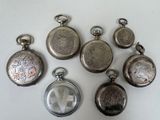 several silver pocket watches are sitting on a white surface