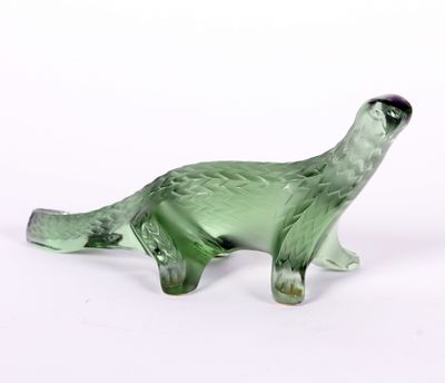 une figurine en verre vert représentant un dinosaure posée sur une surface blanche