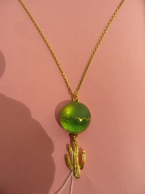 a gold necklace with a green glass bead and a cactus on it