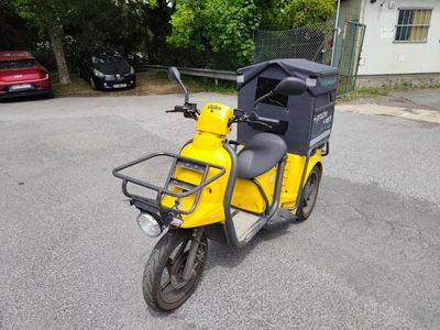 une petite moto jaune garée sur un parking, avec une voiture en arrière-plan