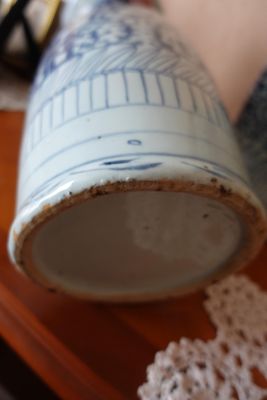 un vase bleu et blanc posé sur une table, à côté d'un napperon en dentelle