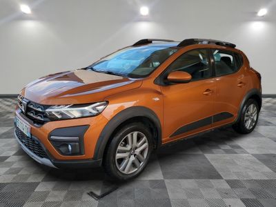 La voiture orange est garée dans une pièce au sol à carreaux.