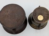 pair of old fashioned metal pots on a white surface with a yellow label