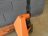 un chariot élévateur orange posé sur un sol en béton, à côté d'un mur de briques