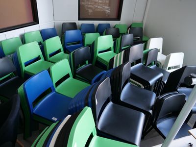 rows of green and blue chairs in a classroom with a chalk board