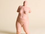 une sculpture rose représentant une femme debout sur une surface blanche