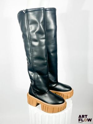 une paire de bottes en cuir noir à semelles en bois posées sur un socle blanc