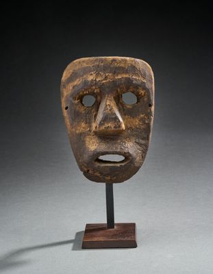 un masque en bois posé sur un socle, sur une surface grise