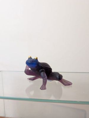 a figurine of a frog sitting on a glass shelf