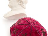 a red velvet kippa with a bust of a man in the background