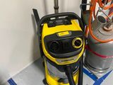 un aspirateur jaune et noir posé par terre à côté d'un bidon d'essence
