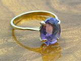 yellow gold ring with a purple stone on a wooden surface
