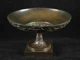un bol antique en bronze posé sur un socle en bois, sur fond noir