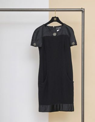 La robe noire est suspendue à un cintre devant un mur jaune.