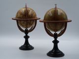 une paire de globes anciens posés sur des socles, sur fond blanc