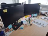 deux écrans d'ordinateur posés sur le bureau, avec des papiers dessus