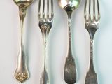 five silver spoons and two silver spoons on a white surface