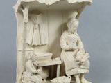 figurine représentant un homme et une femme assis à une table devant une maison de poupées