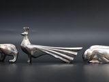 three silver figurines of animals and a bird on a table