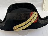 un chapeau de pirate noir orné de bordures dorées et rouges, posé sur une table blanche