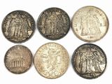 six types différents de pièces d'argent sur une surface blanche