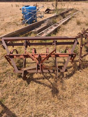 une charrue au milieu d'un champ, avec un tracteur bleu en arrière-plan