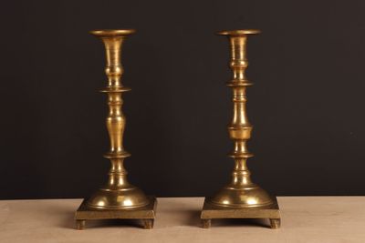 une paire de bougeoirs anciens en laiton posés sur une table, sur fond noir