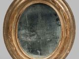 an image of a round mirror with a gold frame on a grey background