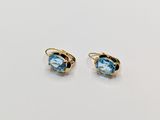 une paire de boucles d'oreilles en topaze bleue posées sur une surface blanche