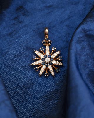a close up of a gold and diamond pendant on a blue cloth