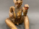 an old wooden statue of a man sitting on the ground holding an apple