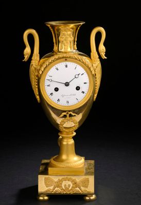 un vase doré orné d'une horloge, sur fond noir