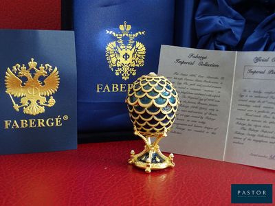 un œuf en or posé sur une table rouge, à côté d'un passeport et d'un sac bleu