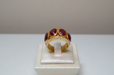 une photo d'une bague en or sertie de pierres rouges, posée sur un écrin blanc