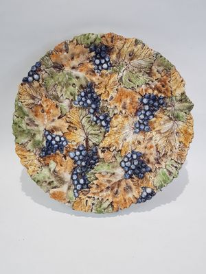 a plate with grapes and leaves on it on a white surface