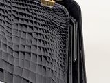 the black crocodile skin handbag is on display against a white background