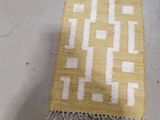 yellow and white area rug with white squares and fringes on the floor