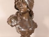 bronze bust of a woman with a hat on her head