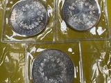 trois pièces d'argent dans des sachets en plastique posées sur une surface jaune