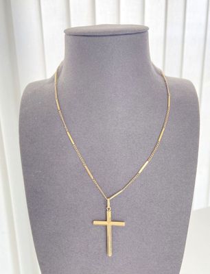 un collier avec une croix en or, présenté sur un mannequin devant une vitrine
