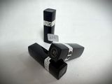 three black lipsticks are lined up on a white surface