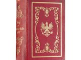 un vieux livre rouge avec des bordures dorées posé sur une surface blanche