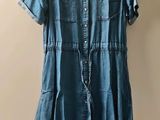 denim dress hanging on a hanger next to a pile of clothes