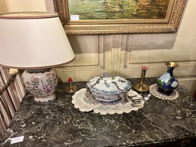 a painting on the wall behind a table with a bowl and a lamp