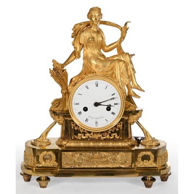 a gold clock with a woman sitting on top of it
